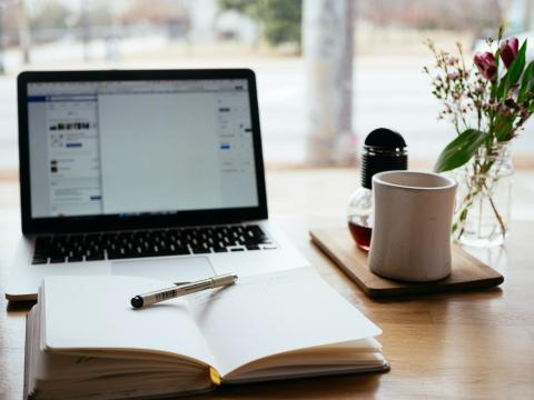 Open notebook in front of a laptop, with a cup of coffee beside on the table