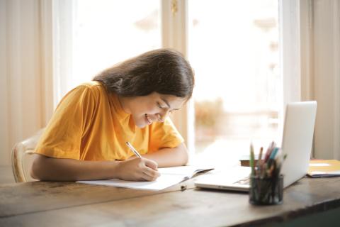 Young woman writing on a notepad in front of a laptop