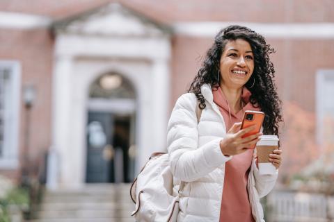 A young woman smiling with her phone in one hand and a takeaway coffee in the other 