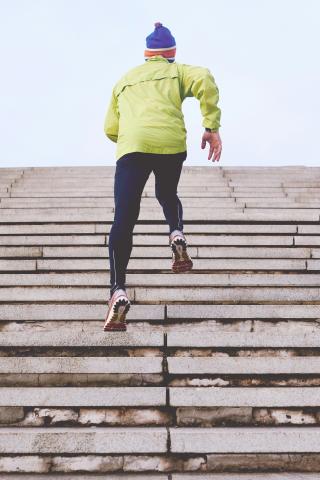 a person in winter running gear, running up a flight of stairs towards an endless blue sky