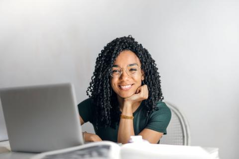 Student sat at a desk with their latop smiling at the camera