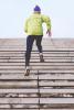 a person in winter running gear, running up a flight of stairs towards an endless blue sky